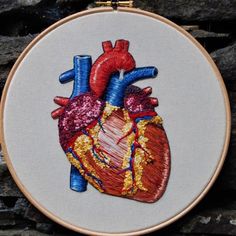 an embroidered heart is shown on a wall hanging in front of a brick wall with orange frame