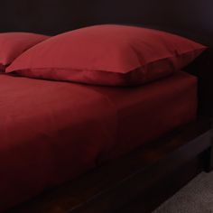 a bed with red sheets and pillows on top of it in a dark colored room