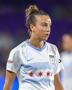 a female soccer player is looking at the ball in her hand as she stands on the field