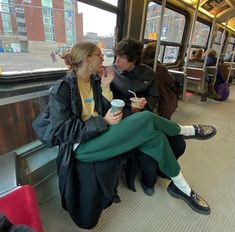 two people sitting on a subway car eating and drinking coffee while looking at each other