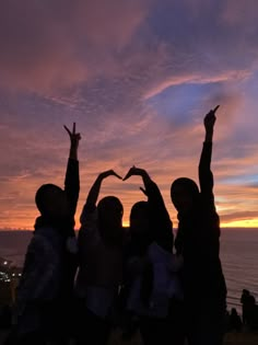 group of people standing together with their arms in the air at sunset by the ocean