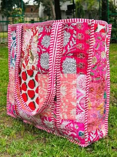 a pink and red patchwork bag sitting in the grass