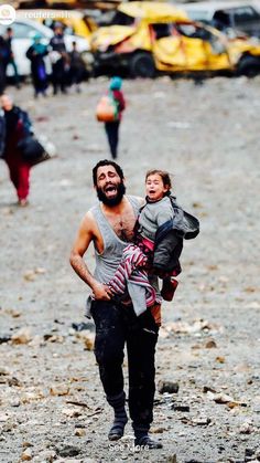 a man carrying a child in his arms while walking on the beach with other people