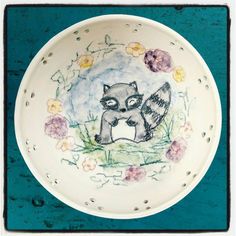 a white bowl with an image of a raccoon and flowers painted on it