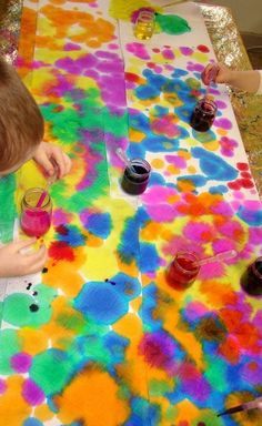 two children are painting on a table covered in colored paper