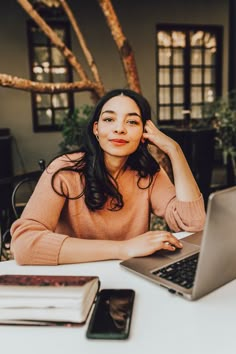 a woman sitting at a table with a laptop and cell phone in front of her