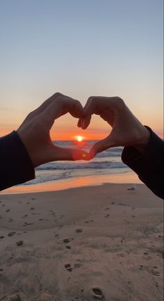 two hands making a heart shape with the sun setting in the background at the beach