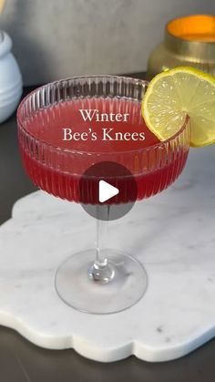 a red drink in a glass with a slice of lemon on the rim that says winter bee's knees