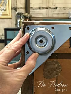 a hand holding a metal object in front of a wooden box with holes and rivets