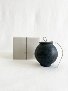 a black vase sitting next to a box on a white surface with the lid open