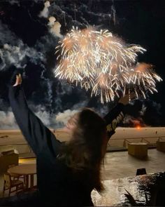 a woman with her arms in the air watching fireworks