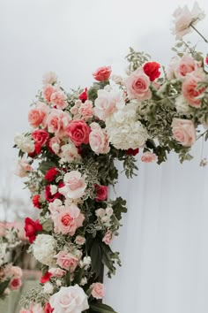 an arrangement of pink and white flowers on the side of a tall pole with greenery