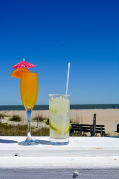 two drinks sitting on top of a white table next to each other near the beach