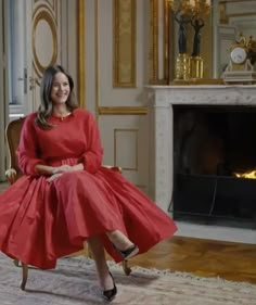 a woman in a red dress sitting on a chair next to a fire place and fireplace