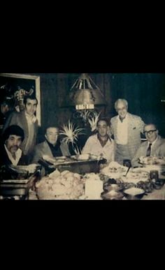 an old black and white photo of men sitting around a table with food on it