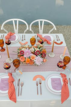 the table is set with orange and pink flowers, silverware, and napkins