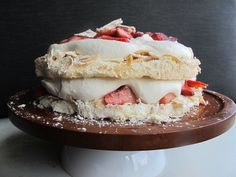 a cake that is sitting on top of a wooden platter with powdered sugar and strawberries