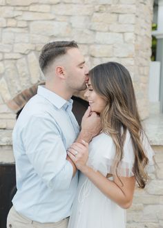 a man and woman standing next to each other in front of a stone wall with a fireplace