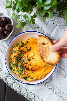 a person is holding a piece of bread over a bowl of eggs and olives