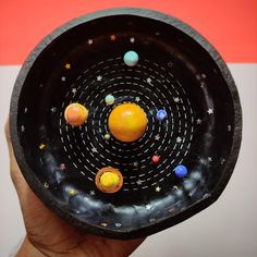 a hand holding a black bowl with planets in it and stars on the outside,