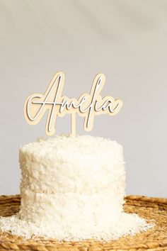 a cake with white frosting and wooden name on top sitting on a wicker basket