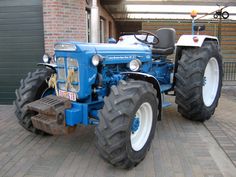 a blue and white tractor parked in front of a brick building next to a garage