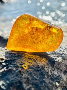 a piece of yellow glass sitting on top of a rock next to the ocean and water