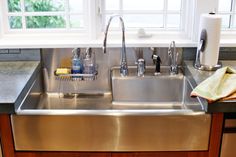 a stainless steel kitchen sink with two faucets in the center and windows above it