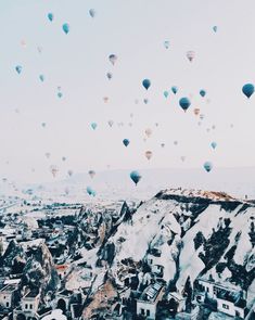 many hot air balloons are flying in the sky over a city with snow covered mountains