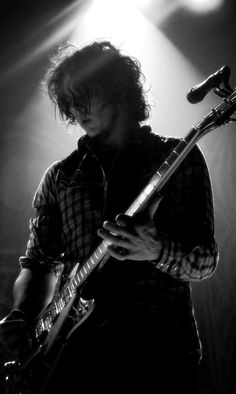 black and white photograph of a man playing guitar in front of spotlights on stage