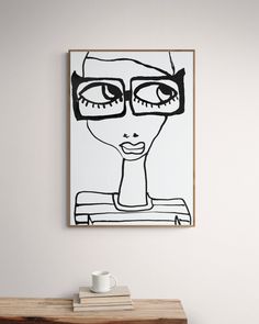 a coffee cup sitting on top of a wooden table in front of a framed drawing