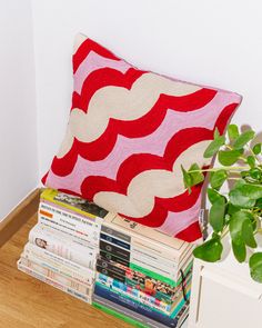 a red and white pillow sitting on top of a pile of books next to a potted plant