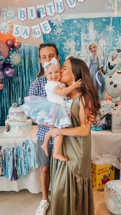 a man and woman holding a baby in front of a frozen princess birthday party backdrop