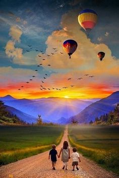 two children walking down a dirt road with hot air balloons in the sky above them