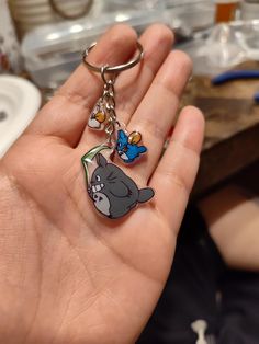 a hand holding two key chains with cartoon characters on them, in front of a sink