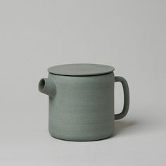 a green cup with a handle on a white surface, sitting in front of a gray background