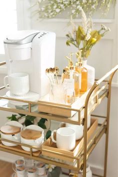 a gold bar cart with cups and mugs on it