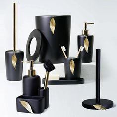 black and gold bathroom accessories are arranged on a white surface with golden leaf accents in the middle