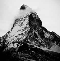 black and white photograph of the top of a mountain with clouds coming out of it