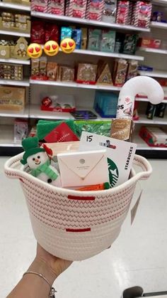 someone is holding up a basket full of christmas items in a store with holiday decorations on the shelves behind them