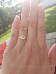 a woman's hand with a diamond ring on top of her finger, in front of a house