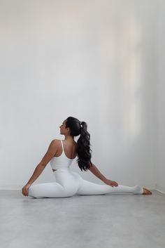 a woman is sitting on the floor in white yoga clothes and has her legs crossed