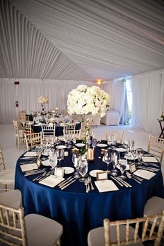 a table set up for an event with blue linens and white flower centerpieces