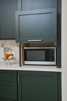 a microwave oven sitting on top of a kitchen counter next to green cabinets and white counter tops