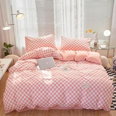 a bed covered in pink and white checkered comforter next to a laptop computer