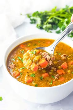 a person holding a spoon over a bowl of soup with meat and vegetables in it