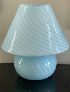 a light blue vase sitting on top of a black table next to a white wall