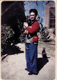 a man holding a cat in his arms while standing next to a building with a bird on it