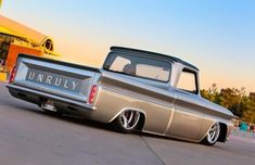 an old pickup truck parked in front of a building with people walking around the parking lot