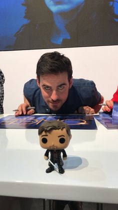 a man looking at a small toy on top of a table next to a poster